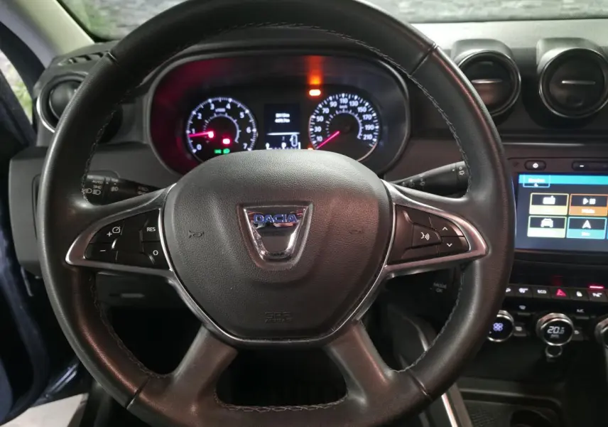 Vue rapprochée du volant noir de Dacia Duster 2019 avec tableau de bord éclairé et écran tactile central visible.