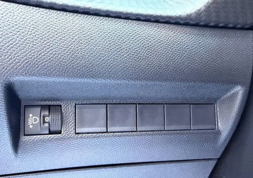 Détail du tableau de bord gris foncé de la Peugeot 208 1.2 100ch, avec commande de réglage des phares.
