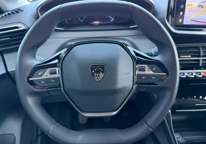 Vue rapprochée du volant cuir noir de la Peugeot 208 2025 avec commandes intégrées et logo lion central.