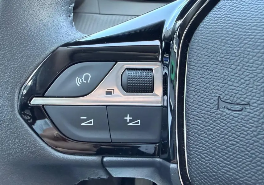 Gros plan sur les commandes noires et argentées du volant de la Peugeot 208 gris Selenium, avec bouton molette et réglages audio.