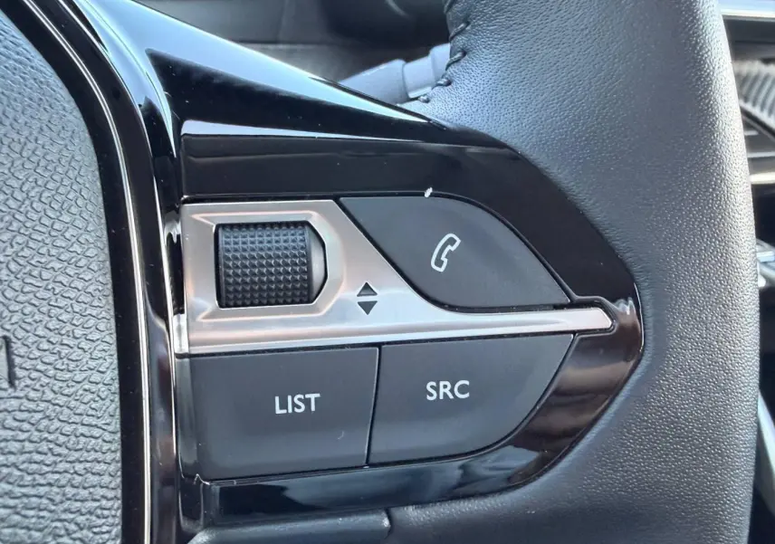 Gros plan sur les commandes audio et téléphone au volant noir de la Peugeot 208 1.2 100ch Allure 2025.