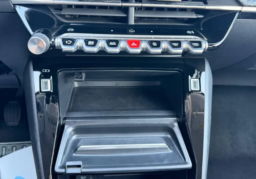 Vue rapprochée de la console centrale noire brillante de la Peugeot 208 2025 avec boutons de commande et prise USB.