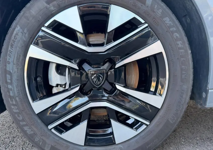 Gros plan sur la jante alu bicolore noire et argentée d’une Peugeot 208 Gris Selenium, avec logo lion central.