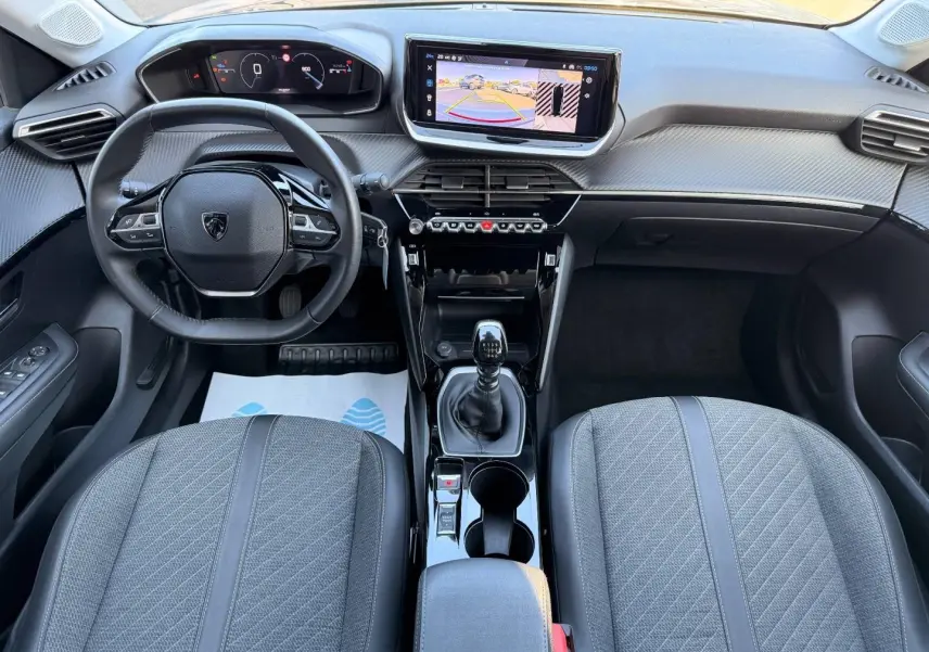 Vue intérieure avant de la Peugeot 208 2025, tableau de bord et volant compact avec écran tactile et levier de vitesse manuel.