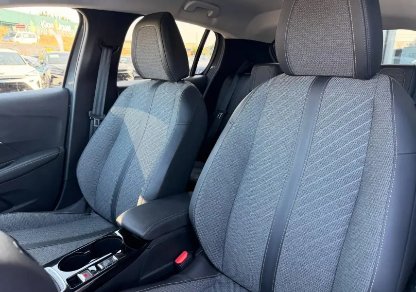 Vue intérieure montrant les sièges avant gris tissu et cuir de la Peugeot 208 1.2 100ch Allure 2025, avec accoudoir central.