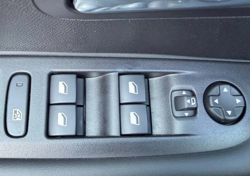 Gros plan sur les commandes de lève-vitres et réglages des rétroviseurs côté conducteur d'une Peugeot 208 gris Selenium.