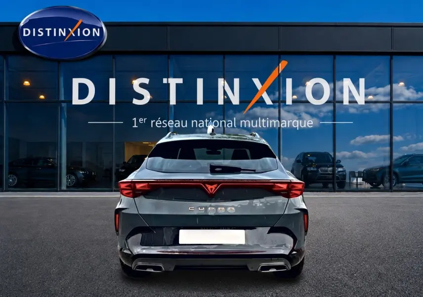 Vue arrière d'un CUPRA Formentor bleu fjord garé devant une vitrine Distinxion, avec feux arrière LED et double sortie d'échappement.