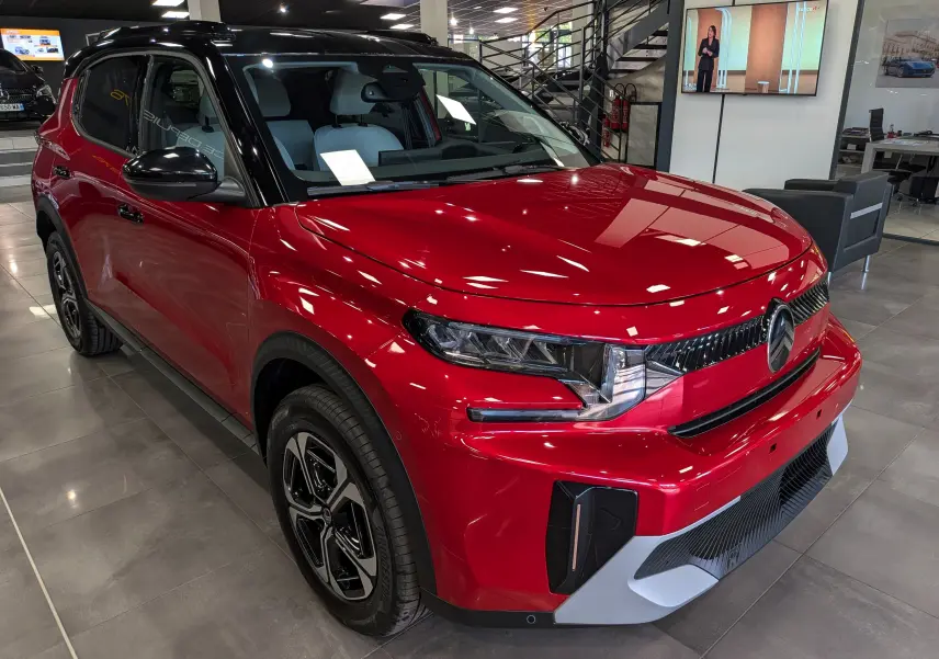 Vue 3/4 avant droite d'une Citroën C3 Aircross hybride rouge Elixir avec toit noir en showroom intérieur.