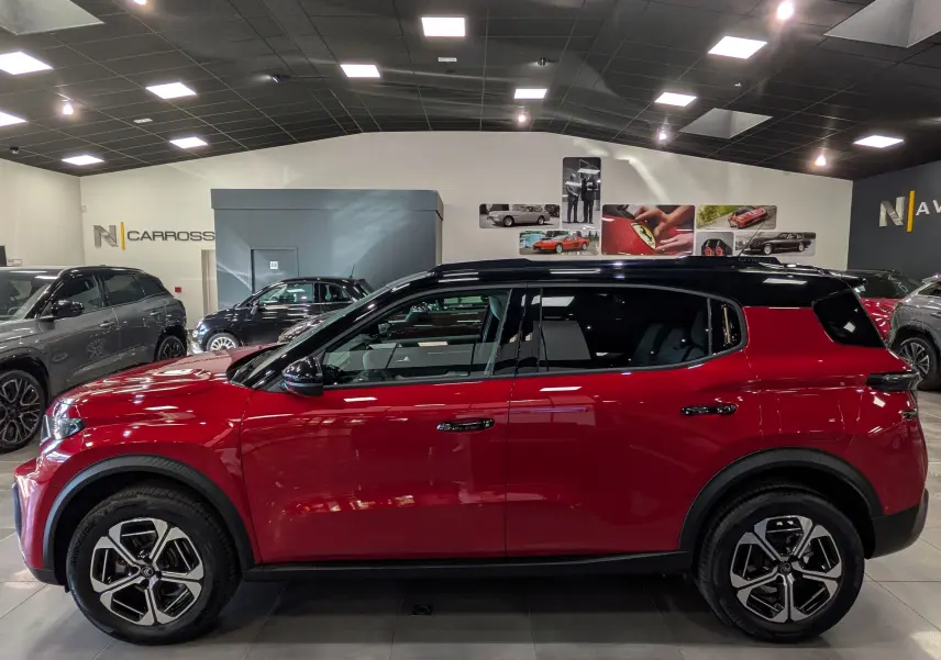 Vue de profil droit d'un Citroën C3 Aircross 2026 rouge Elixir avec toit noir dans un showroom.