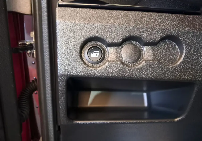 Bouton d'ouverture du coffre sur la portière côté conducteur d'une Aixam Ambition rouge vue de près.