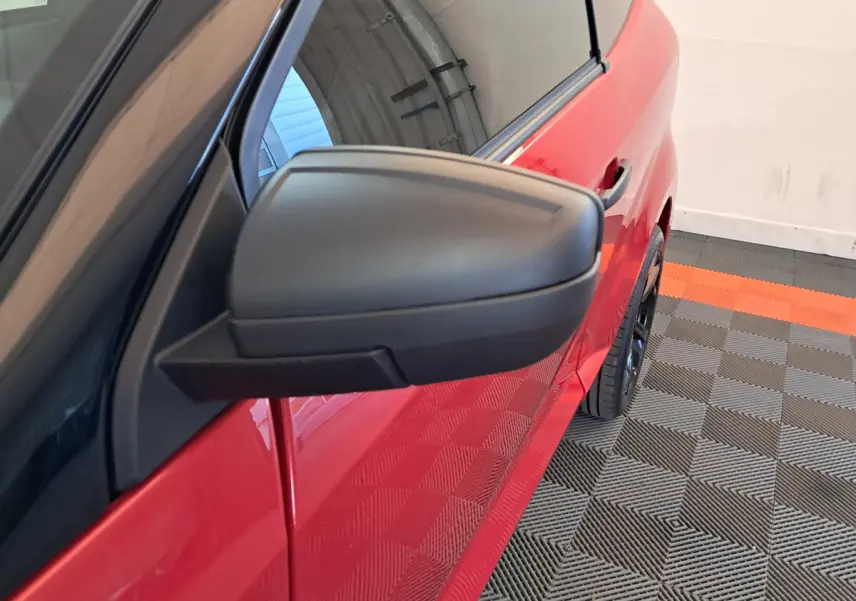 Rétroviseur côté conducteur en gros plan sur la portière rouge d'une Aixam Ambition 2025 stationnée intérieurement.