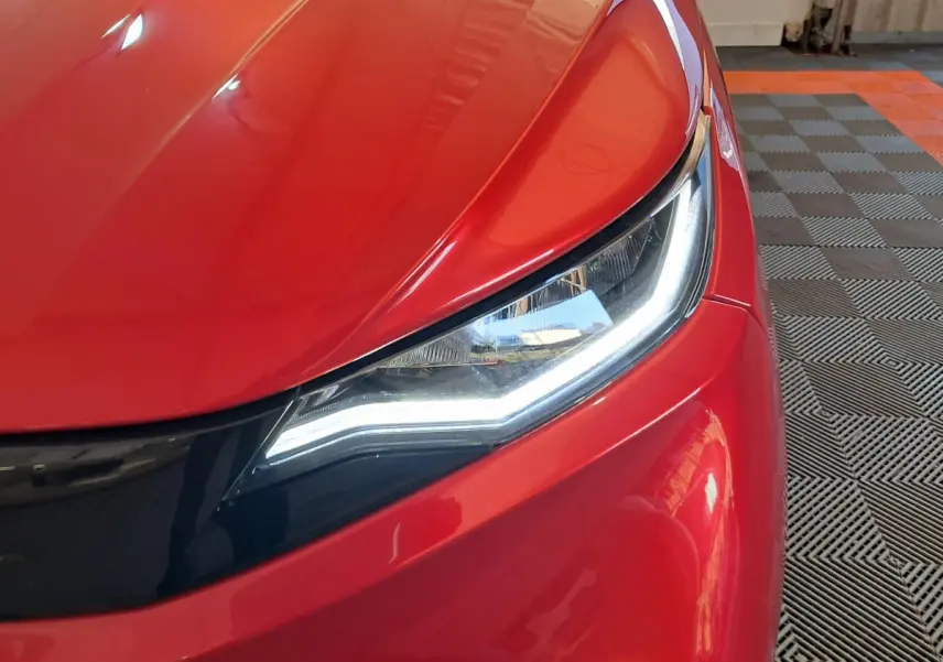 Gros plan sur le phare avant droit d'une AIXAM AMBITION rouge 2025 avec éclairage LED et carrosserie brillante.