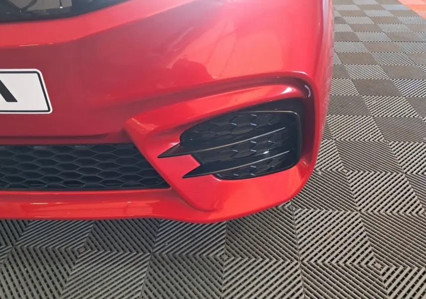 Gros plan sur l'angle avant droit rouge de l'AIXAM AMBITION 2025 avec une grille noire et un éclairage distinctif.