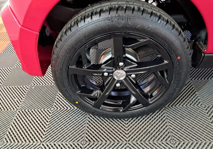 Gros plan sur la roue avant gauche noire brillante d'une Aixam Ambition rouge, soulignant la jante sportive cinq branches.