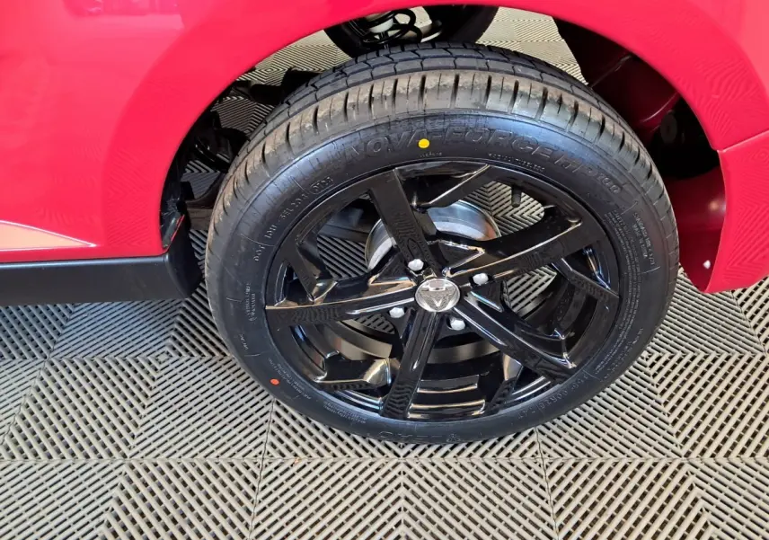 Gros plan sur la roue arrière droite noire brillante d'une AIXAM Ambition rouge 2025 avec jante sport cinq branches.