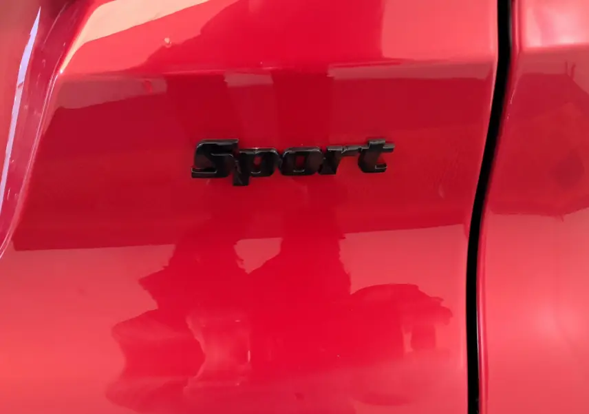 Gros plan sur l'emblème "Sport" noir sur la porte rouge vif de l'AIXAM AMBITION 2025 côté conducteur.