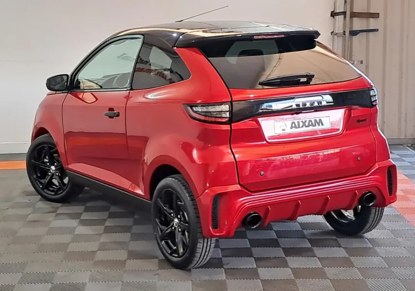 Vue 3/4 arrière droite d'une Aixam Ambition rouge avec jantes noires et toit noir brillant dans un garage.