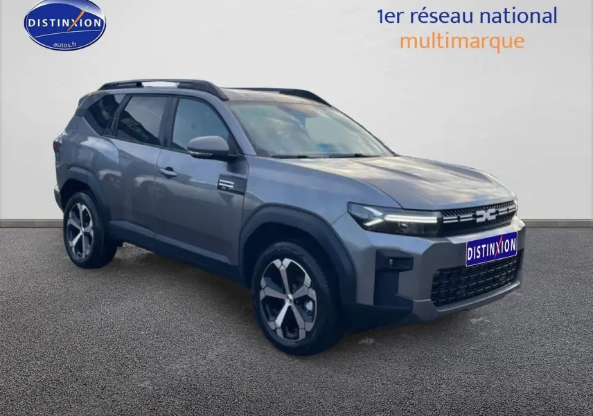 SUV Dacia Bigster gris schiste en 3/4 avant droit, avec jantes alliage diamantées et barres de toit noires.