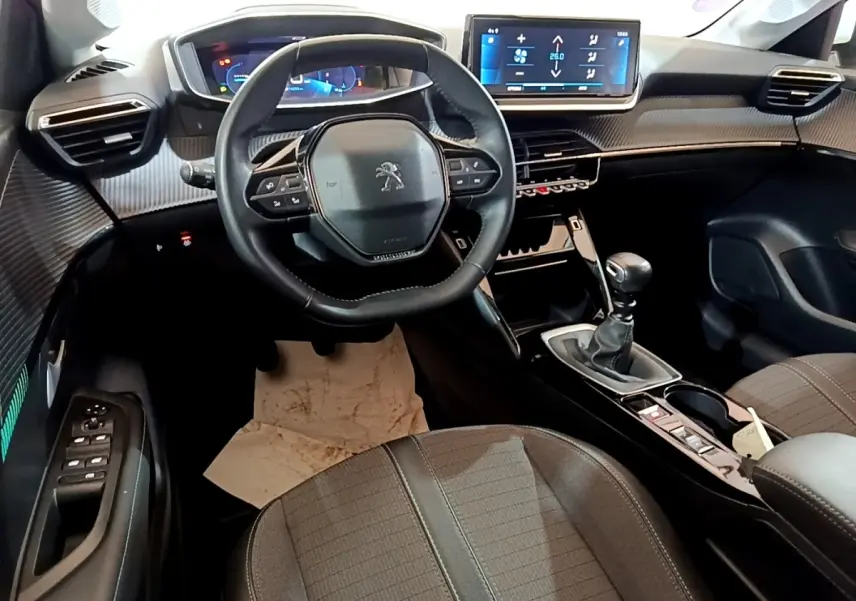 Vue intérieure avant de la Peugeot 208 PureTech 100, tableau de bord noir avec écran tactile et volant cuir multifonctions.