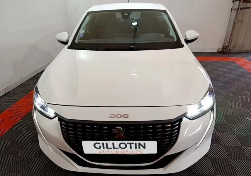 Vue avant d'une Peugeot 208 blanche avec phares LED allumés dans un garage.