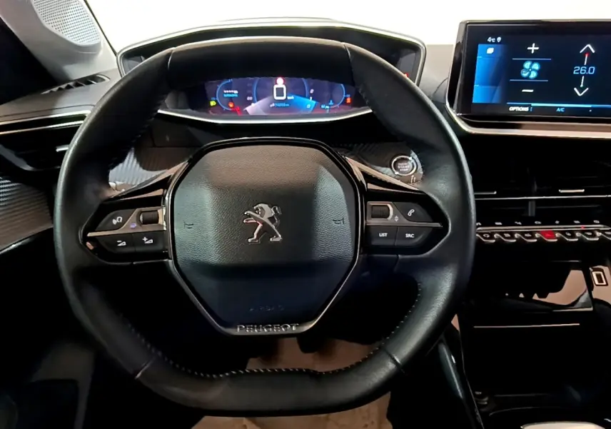 Vue intérieure centrée sur le volant cuir noir de la Peugeot 208 PureTech 100 avec tableau de bord digital et écran tactile.