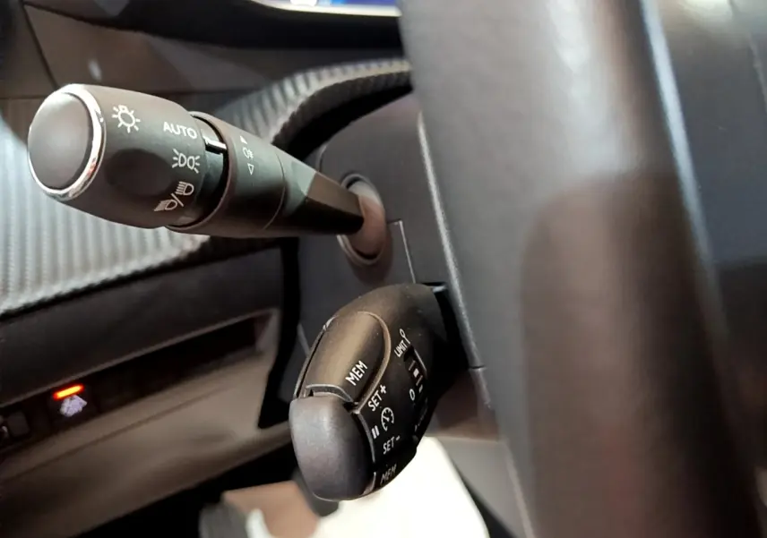 Gros plan sur la commande des phares et régulateur de vitesse du volant d'une Peugeot 208 blanche, vue côté conducteur.
