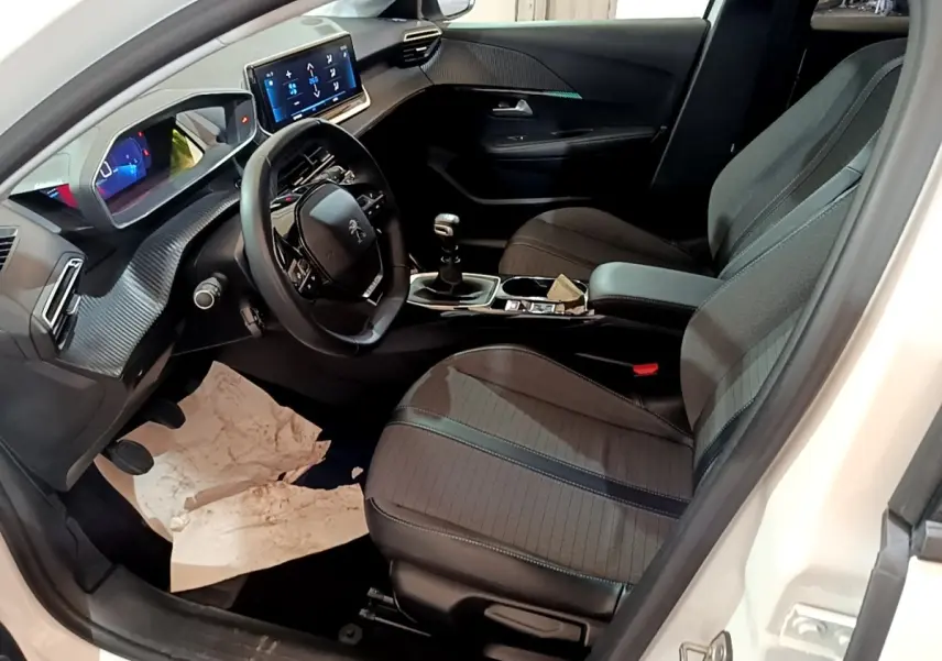Vue intérieure côté conducteur de la Peugeot 208 blanche, montrant le volant cuir, tableau de bord digital et écran tactile central.