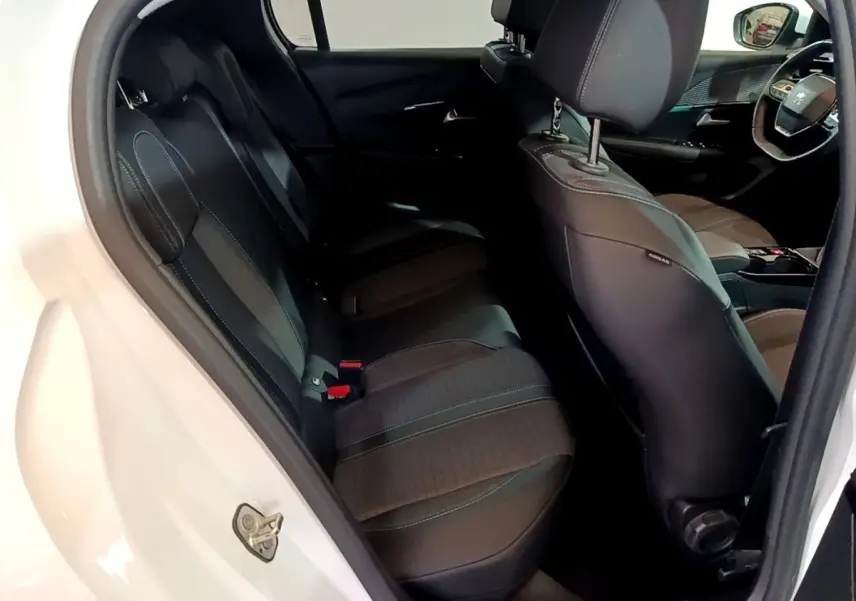 Vue intérieure côté gauche arrière de la Peugeot 208 blanche, montrant les sièges noirs et le volant multifonctions.