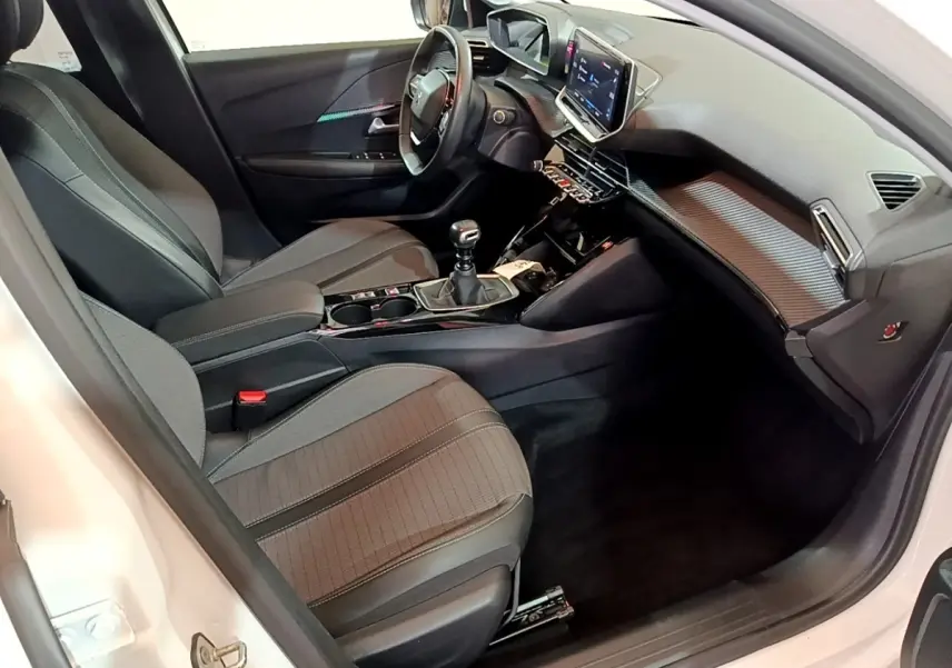 Vue intérieure côté conducteur de la Peugeot 208 blanche, montrant le tableau de bord et la console centrale avec écran tactile.