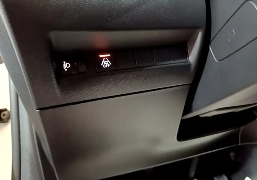 Gros plan sur les commandes noires sous le tableau de bord d'une Peugeot 208 blanche, avec témoin d'alerte allumé.