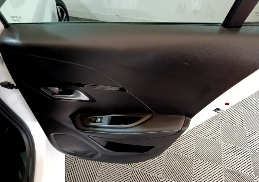 Gros plan sur la porte avant gauche noire d'une Peugeot 208 blanche, mettant en valeur la poignée et les commandes de vitre.
