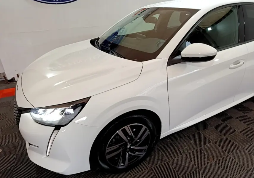Peugeot 208 blanc vue 3/4 avant droit avec phares LED allumés et jantes alliage noires.