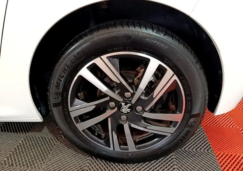 Gros plan sur la roue avant gauche blanche d'une Peugeot 208 avec jante alliage noire et argentée au logo lion.