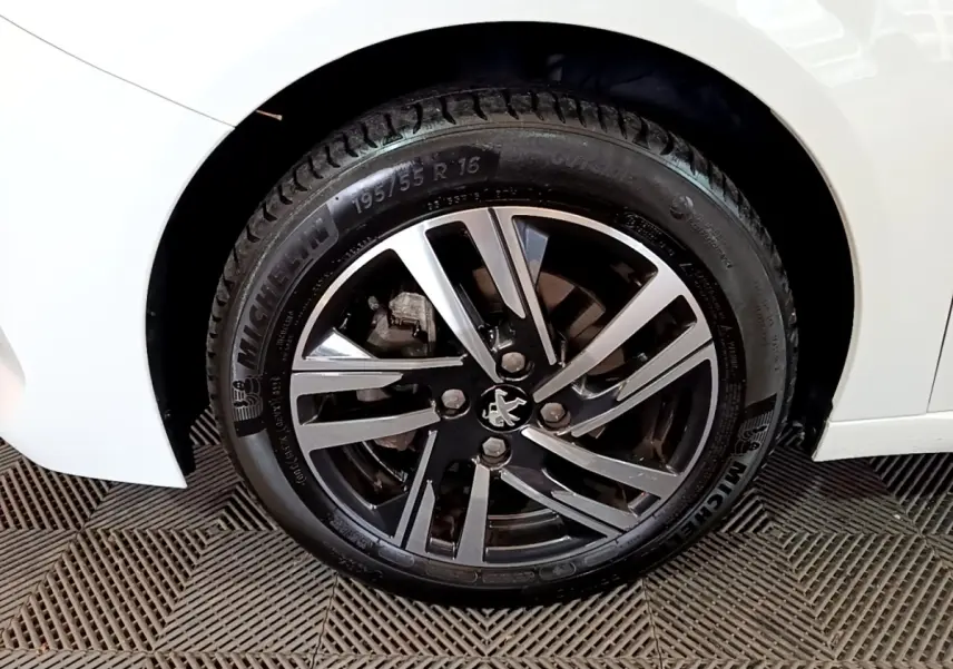 Gros plan sur la roue avant droite d'une Peugeot 208 blanche, jante alliage noire et argent avec logo lion central.