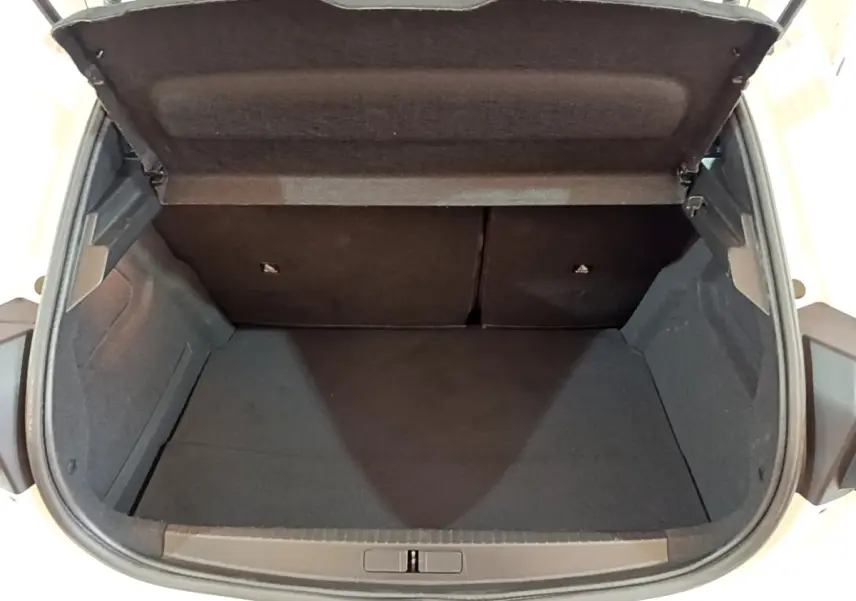 Coffre ouvert vu de l'arrière d'une Peugeot 208 blanche, montrant l'espace de chargement vide et les sièges rabattables.