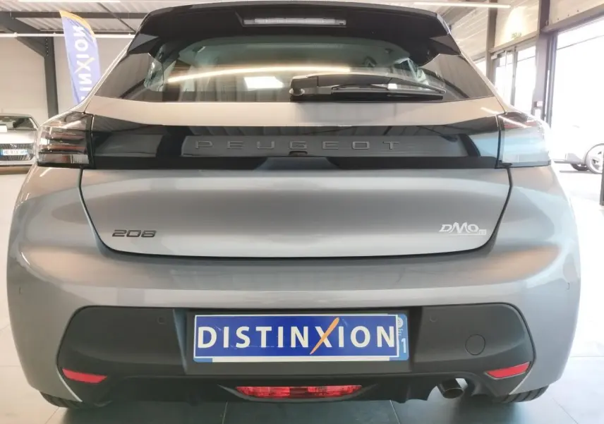 Vue arrière d'une Peugeot 208 2024 gris Artense avec logo distinctif et plaque d'immatriculation Distinxion en intérieur showroom.