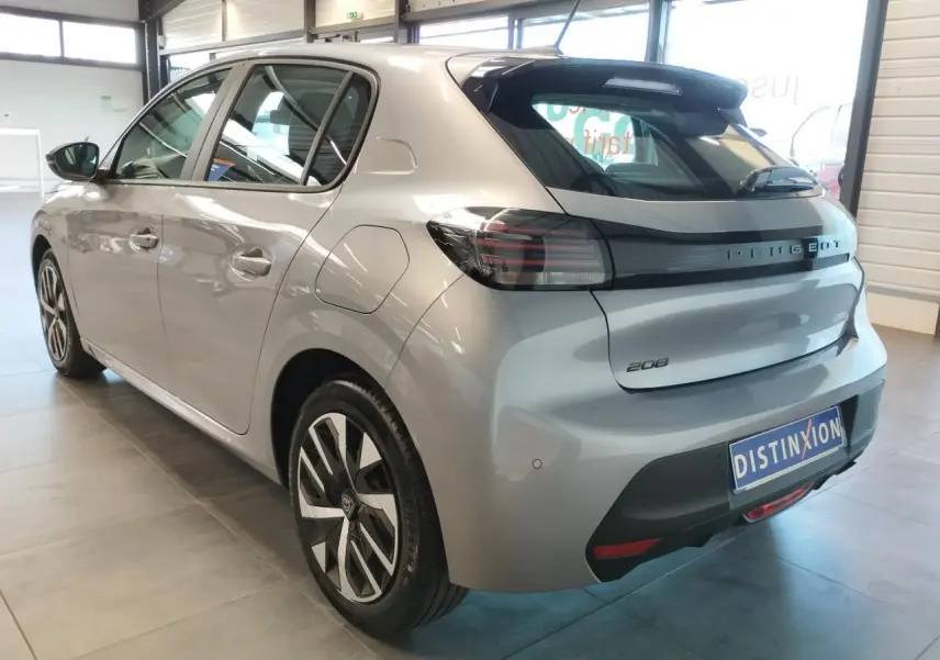 Vue 3/4 arrière droite d'une Peugeot 208 2024 gris Artense avec feux arrière noirs et jantes bicolores en concession.