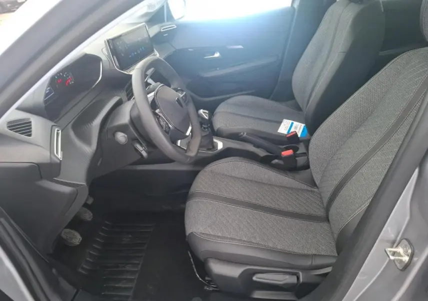 Intérieur avant droit de la Peugeot 208 gris clair 2024, montrant les sièges tissu, volant compact et boîte manuelle.