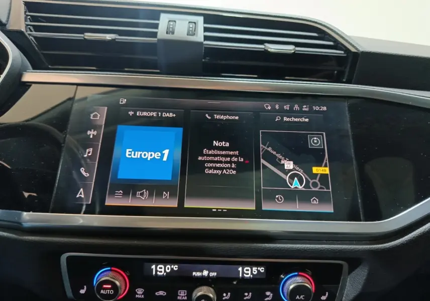 Écran tactile central de l'Audi Q3 Sportback gris foncé, affichant navigation et radio, avec commandes climatisation en dessous.