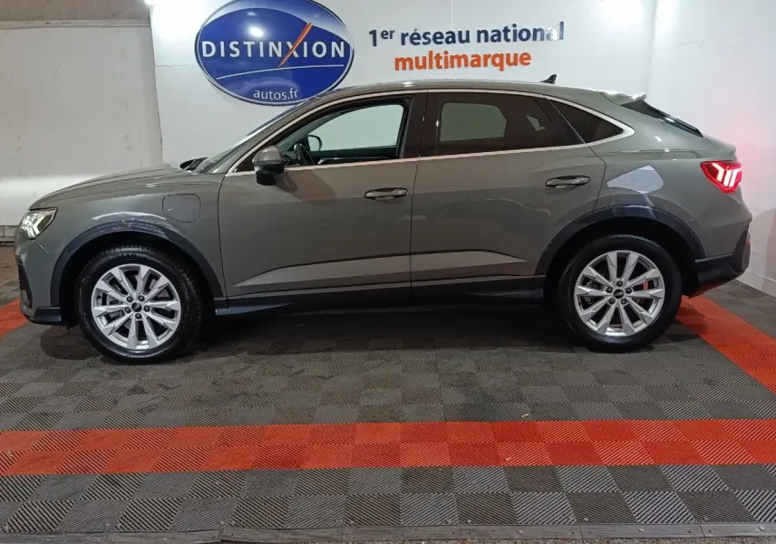 Audi Q3 Sportback gris foncé vue de profil côté gauche, avec jantes alliage et feux arrière allumés.