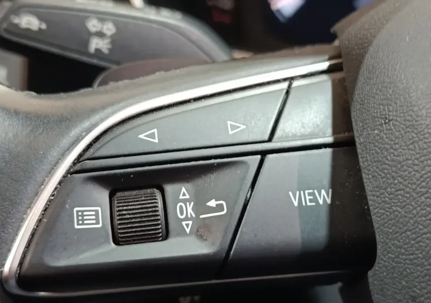 Gros plan sur les commandes multifonctions noires du volant de l'Audi Q3 Sportback hybride rechargeable, détails des boutons et molette.