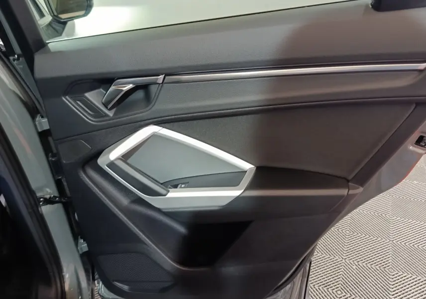 Vue intérieure de la porte avant gauche gris foncé de l'Audi Q3 Sportback 45 TFSI e avec poignée argentée et commandes vitres.
