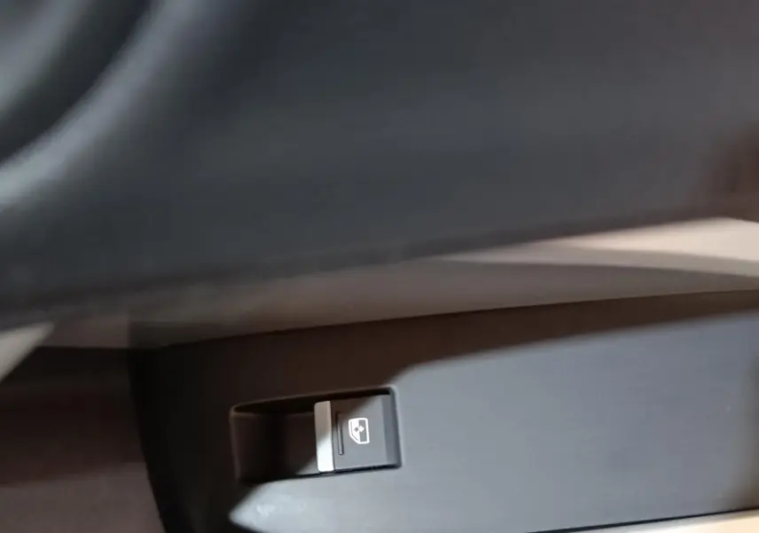 Gros plan sur le bouton de commande de la vitre électrique côté conducteur dans l’habitacle d’un Audi Q3 Sportback gris foncé.
