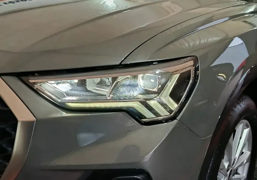 Gros plan sur le phare avant droit gris foncé de l'Audi Q3 Sportback 45 TFSI e avec jante visible.
