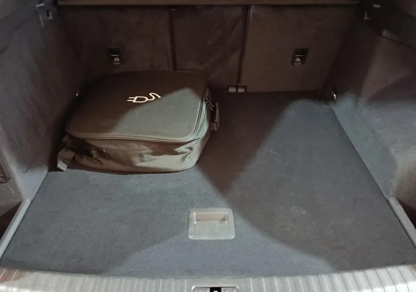Coffre ouvert vu de face de l’Audi Q3 Sportback gris foncé avec sac de charge hybride posé à gauche.