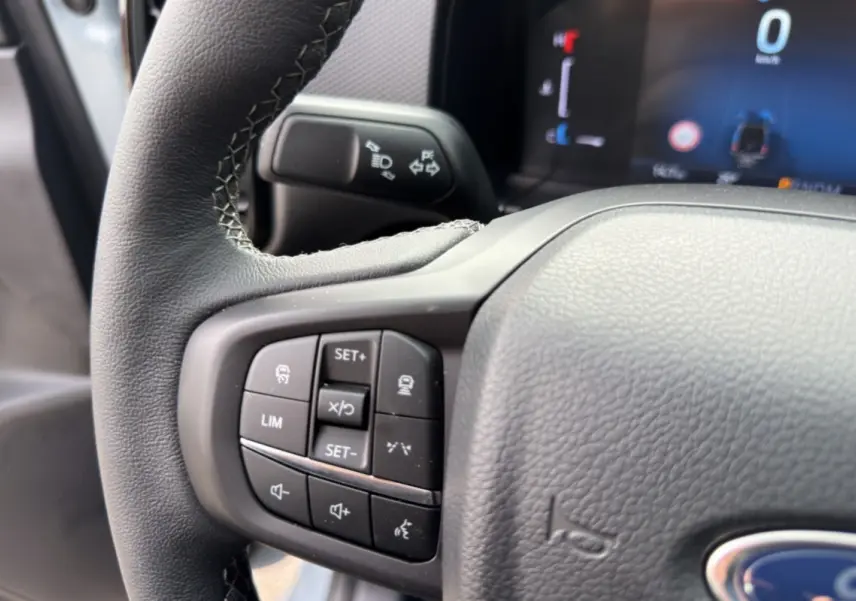 Gros plan sur les commandes multifonctions du volant cuir du Ford Ranger gris commandeur, tableau de bord numérique en arrière-plan.