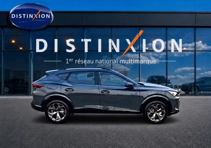 Vue latérale gauche du CUPRA Formentor 1.5 etsi hybrid 150 DSG7 en bleu fjord avec jantes 18 pouces devant un showroom Distinxion.
