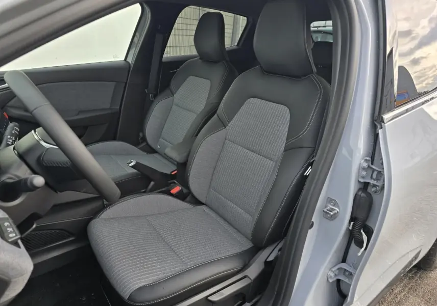 Vue intérieure côté conducteur de la Renault Clio gris Rafale, montrant les sièges bi-matière gris et noir avec surpiqûres blanches.