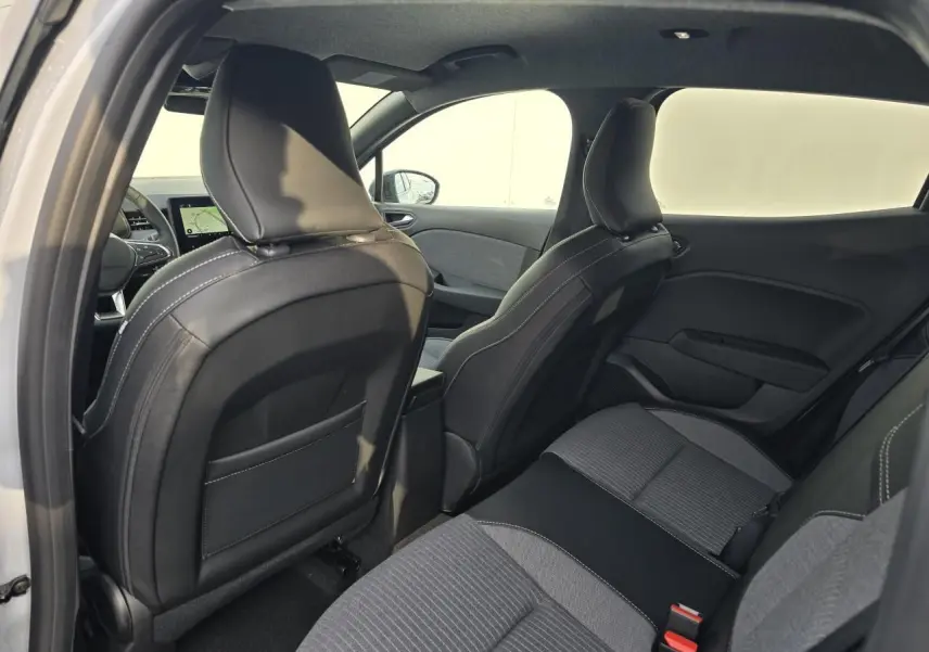 Vue intérieure arrière droite de la Renault Clio 2025, sièges tissu gris mélangé avec surpiqûres blanches et accoudoir central.