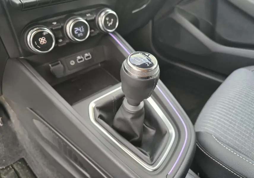 Gros plan sur la boîte manuelle et la console centrale noire avec éclairage d'ambiance violet dans une Renault Clio gris Rafale.